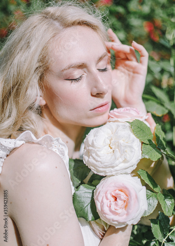  Beautiful blonde young woman enjoying smell in a rose garden. Beautiful big roses flowers. Dreaming young model between flowers