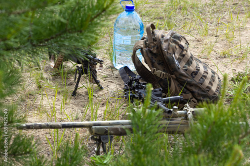 Three rifles, backpack and bottle of water on the ground in the forest, army weapon of active military game airsoft
