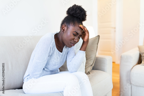 African American Woman in painful expression holding hands against belly suffering menstrual period pain, lying sad on home bed, having tummy cramp in female health concept