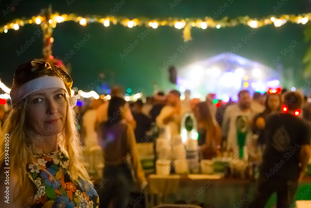 woman in yellow santa claus hat smiling, in the background festive lights of new year