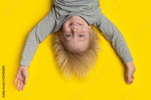 Funny boy with blond hair hanging upside down. Yellow background. Happy boy photo