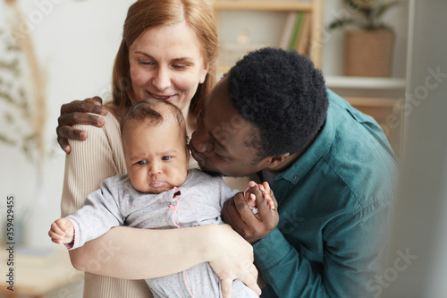 Waist up portrait of loving interracial family at home, focus on African-American man kissing cute mixed race baby © Seventyfour