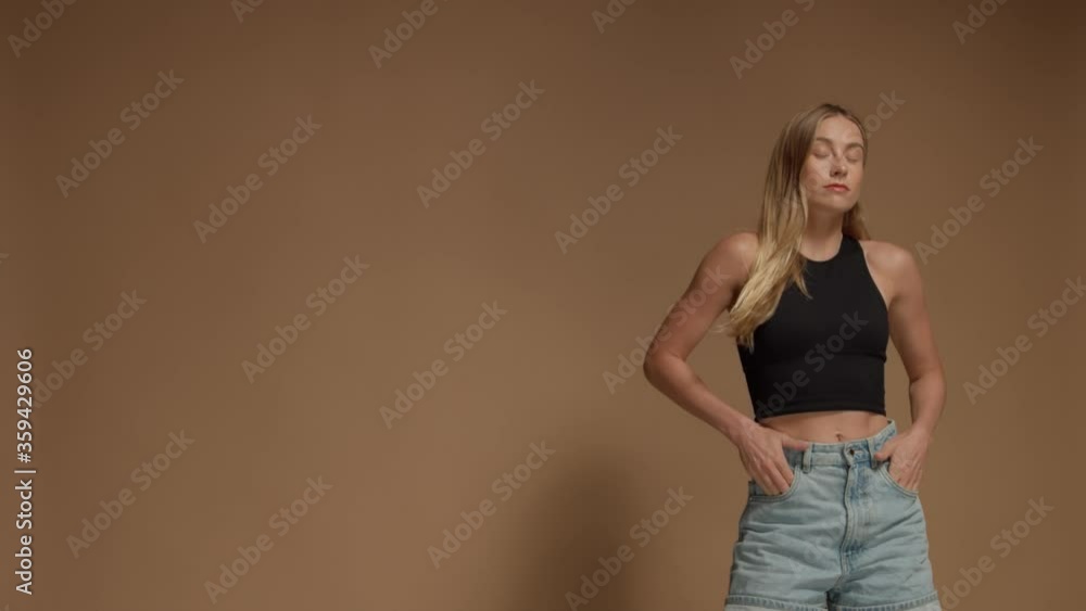 Young woman with blonde long hair on beige warm background in studio poses to another camera Young woman with blonde long hair on beige warm background in studio poses to another camera