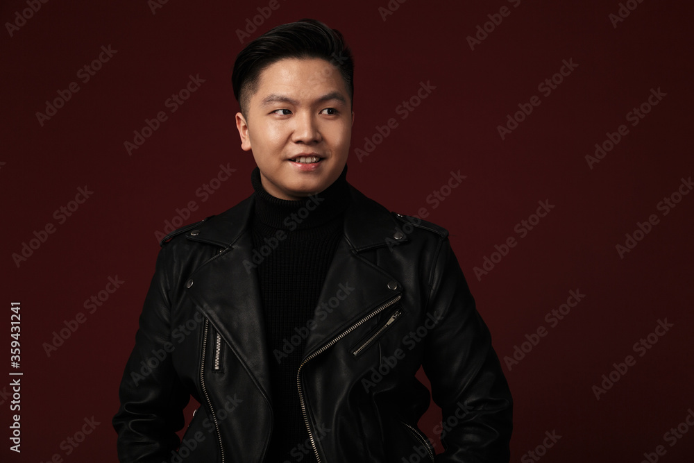 Image of joyful asian man in leather jacket smiling and looking aside Image of joyful asian man in leather jacket smiling and looking aside