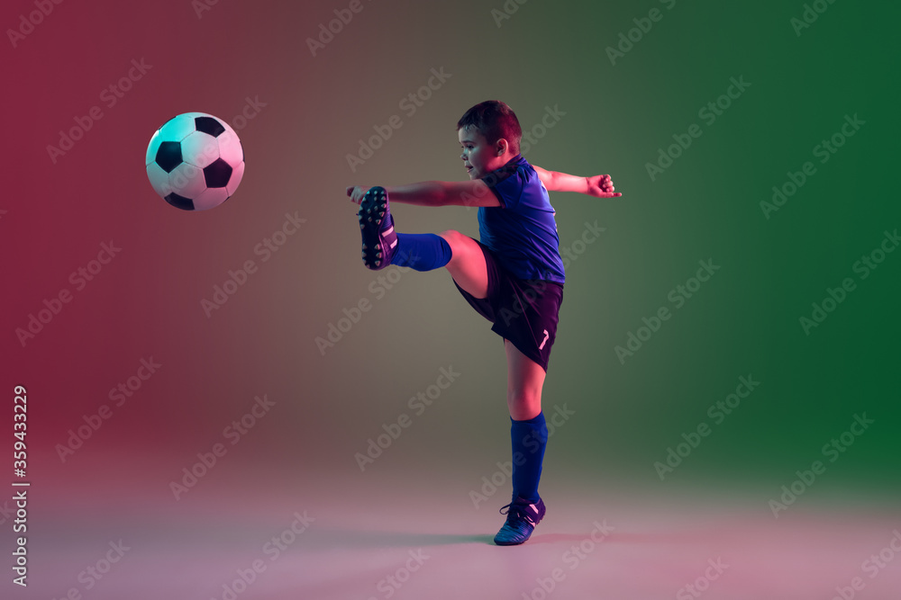 Emotions. Teen male football or soccer player on gradient background in neon light. Caucasian boy training, practicing on the run, in jump. Concept of sport, competition, winning, motion, action.