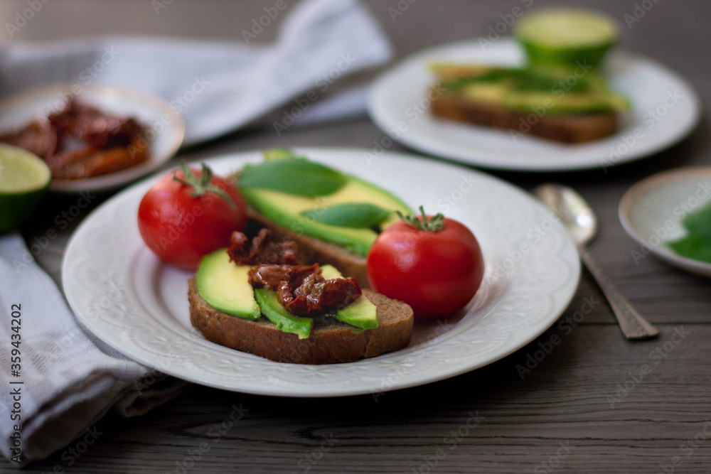 Bruschetta style rye bread toasts with avocado, sun-dried tomatoes, basil, dill and lime. Rustic dark wooden background Bruschetta style rye bread toasts with avocado, sun-dried tomatoes, basil, dill and lime. Rustic dark wooden background