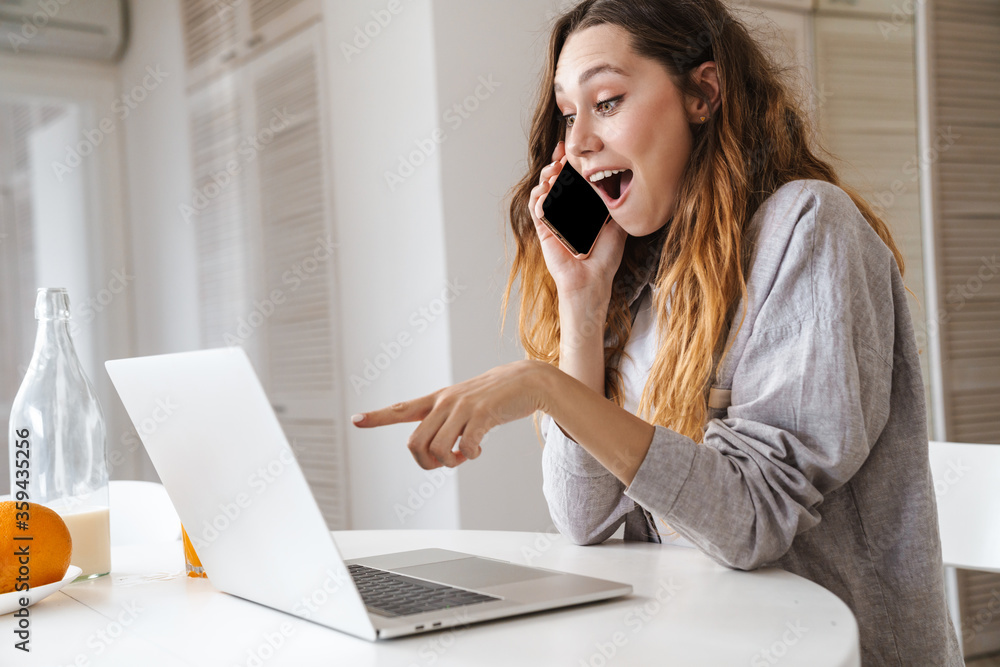 Portrait of woman pointing finger at laptop and talking on cellphone Portrait of woman pointing finger at laptop and talking on cellphone