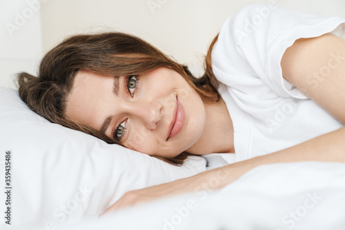 Image of beautiful caucasian woman smiling while lying in bed