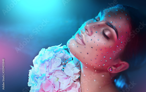 Beauty fashion Woman face decorated with gem stones, crystals, diamonds Closeup Art Portrait with Hydrangea flower. Model girl, holiday Glamour shiny make up with gems, jewellery, jewelry, accessories