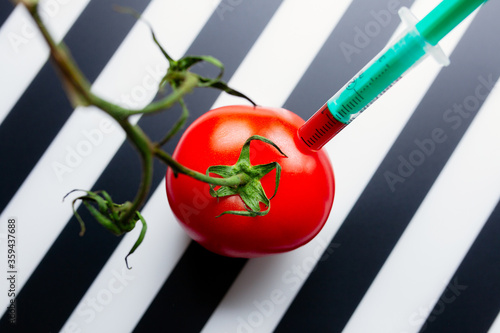 Red tomato with green stem on a striped black and white background stabbed with medical syringe, GMO food concept photo