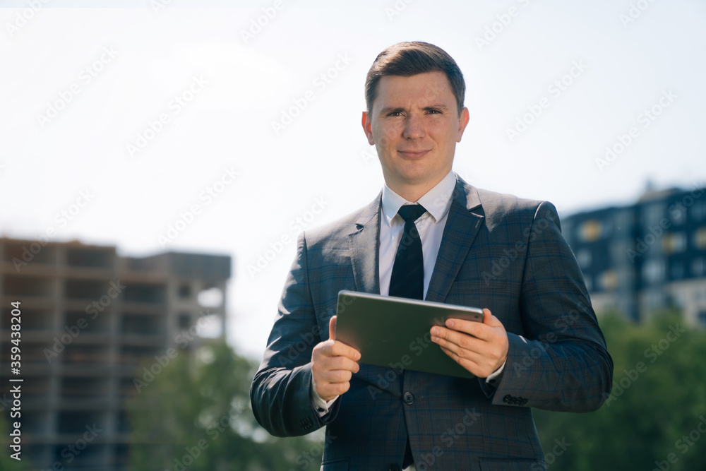 Stylish young man holds a digital tablet against the backdrop of the city background. The Stylish young man holds a digital tablet against the backdrop of the city background. The