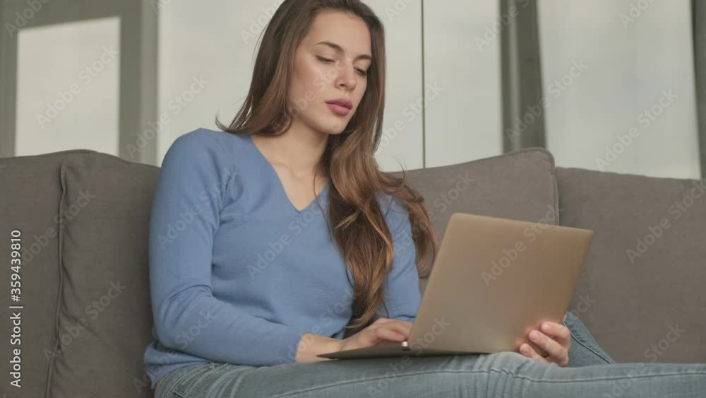 A serious nice woman is working with laptop while sitting on sofa at the living room A serious nice woman is working with laptop while sitting on sofa at the living room