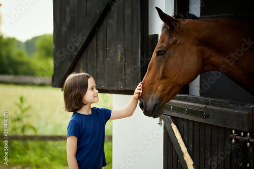 Fototapeta Naklejka Na Ścianę i Meble -  Little girl strokes a beautiful horse in the barn