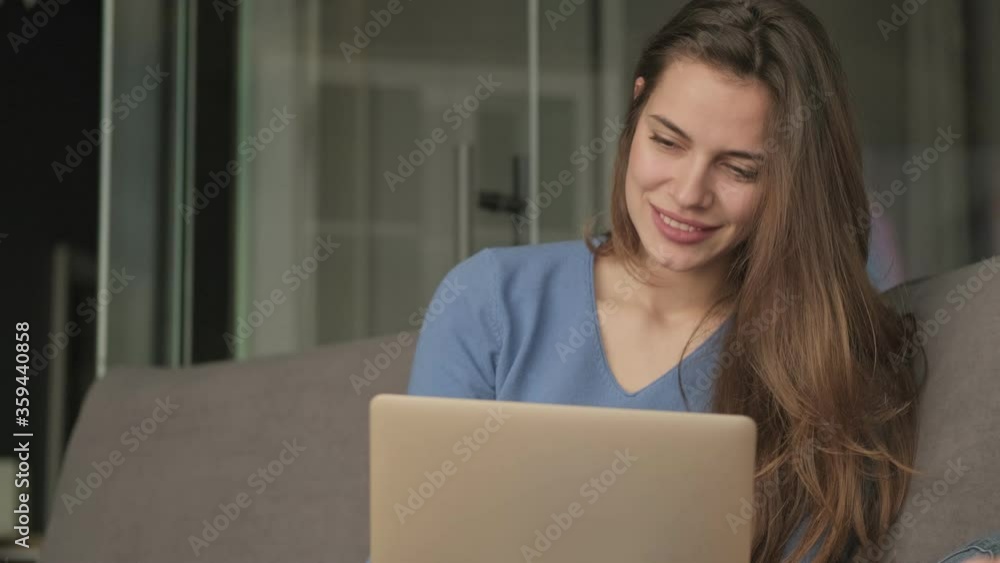 A positive smiling woman is using her laptop while sitting on the sofa in the living room A positive smiling woman is using her laptop while sitting on the sofa in the living room