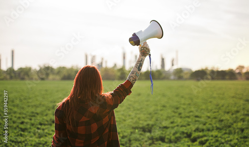 Tableau sur toile Rear view of woman activist with megaphone outdoors by oil refinery, protesting
