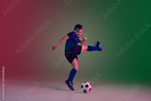 Winner. Teen male football or soccer player on gradient background in neon light. Caucasian boy training, practicing on the run, in jump. Concept of sport, competition, winning, motion, action. © master1305