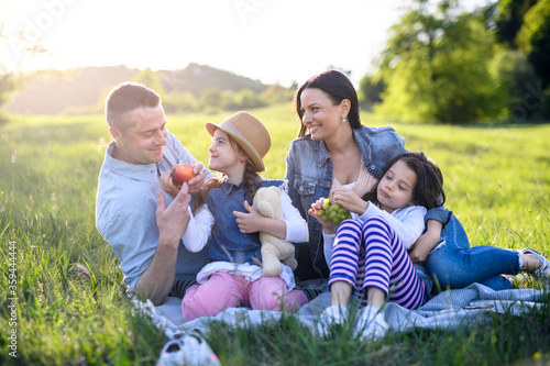 Happy family with two small daughters sitting outdoors in spring nature, having picnic. © Halfpoint