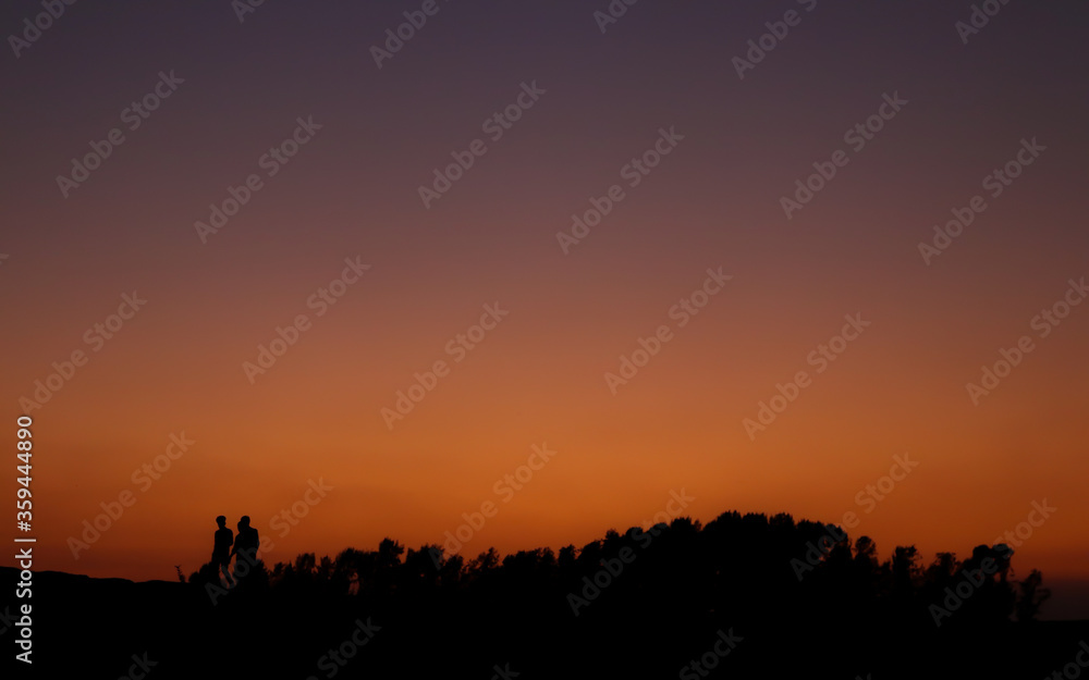 People walking under the orange sky after sunset