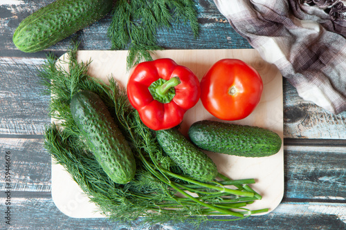 vegetables, Bulgarian peppers, dill, cucumbers on a light cutting Board, dark wooden background