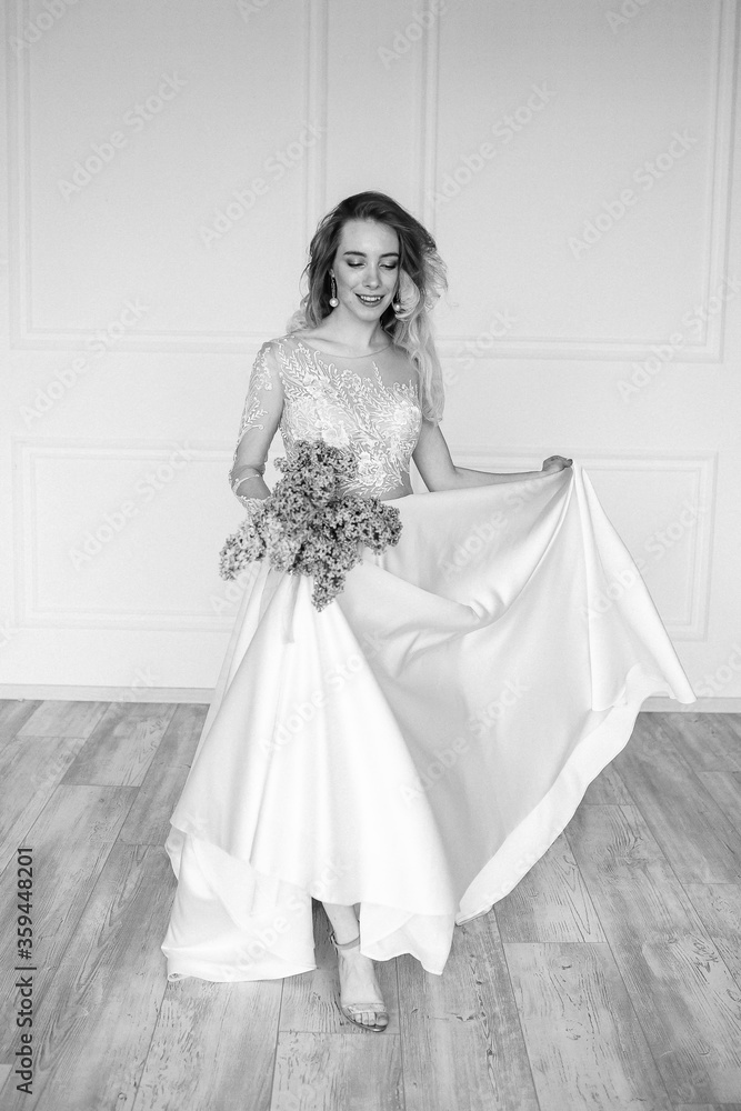 Beautiful girl woman bride in a delightful wedding dress with a bouquet of flowers dancing in front of a mirror portrait of a blonde with blue eyes holding Beautiful girl woman bride in a delightful wedding dress with a bouquet of flowers dancing in front of a mirror portrait of a blonde with blue eyes holding
