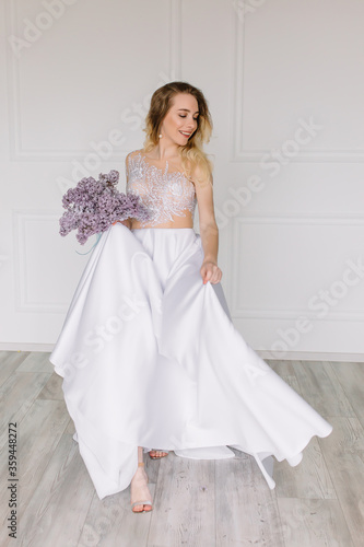 Beautiful girl woman bride in a delightful wedding dress with a bouquet of flowers dancing in front of a mirror portrait of a blonde with blue eyes holding