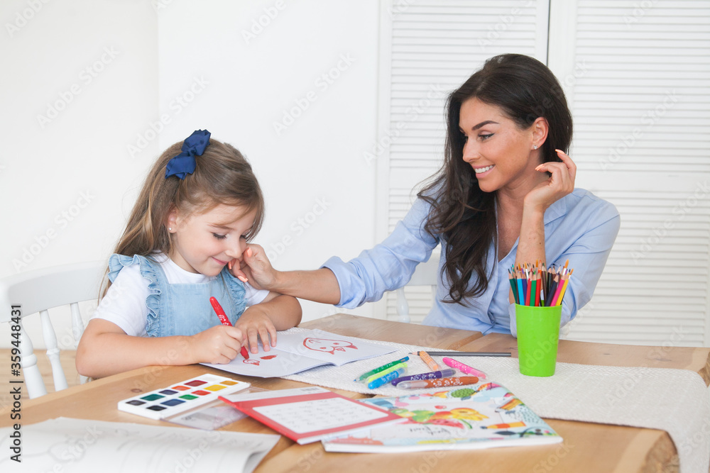 Smiling mother and daughter preparing for lessons and draws at the table with pencils and paints. Parent and pupil of preschool. First day of fall autumn. Girl from elementary class, back to school Smiling mother and daughter preparing for lessons and draws at the table with pencils and paints. Parent and pupil of preschool. First day of fall autumn. Girl from elementary class, back to school