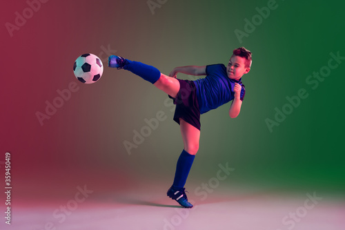 Fototapeta Naklejka Na Ścianę i Meble -  Leader. Teen male football or soccer player on gradient background in neon light. Caucasian boy training, practicing on the run, in jump. Concept of sport, competition, winning, motion, action.