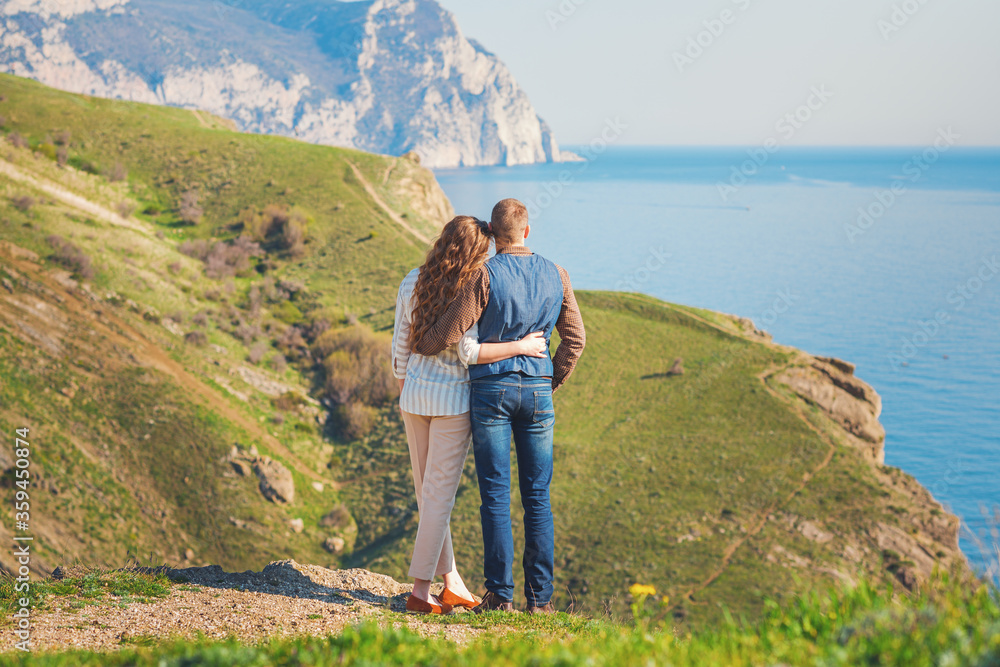 Naklejka premium Young couple in love outdoor.Stunning sensual outdoor portrait of young stylish fashion couple posing on the background of mountains and sea