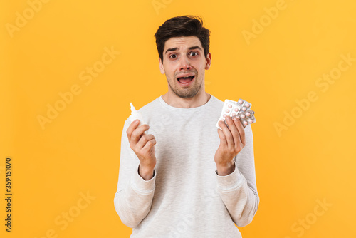 Photo of unhappy man with allergy posing with pills and nose drop