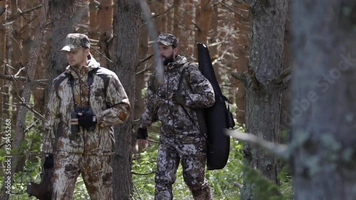 Two hunter men in camouflage clothes with guns walking through forest during hunting season. Man hunter outdoor in forest hunting. Male Tourists. Slow motion
