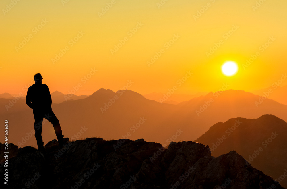 Happy success winning man standing relaxed on mountain at sunset. Border region of Tyrol, Austria and Allgaeu, Bavaria, Germany.