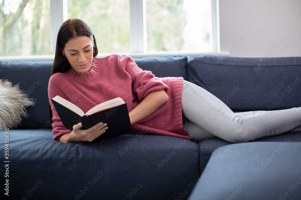 Obraz premium Woman Relaxing Lying On Sofa At Home Reading Book