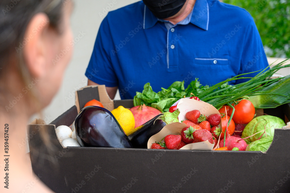 Delivery man in black mask with groceries box handing it to the customer. Online orders during social distancings Delivery man in black mask with groceries box handing it to the customer. Online orders during social distancings