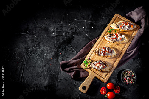 Bruschetta with tomatoes, mozzarella cheese and basil on dark background. Traditional italian appetizer or snack, antipasto