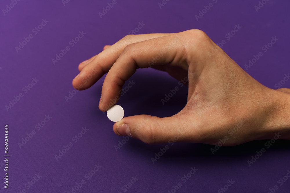 Hand holding a pill on a purple background. Hand holding a pill on a purple background.