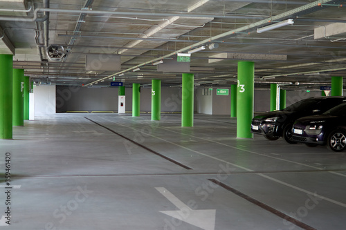 Underground empty parking garage with overhead lights and an exit sign hanging from the ceiling. Free parking for cars