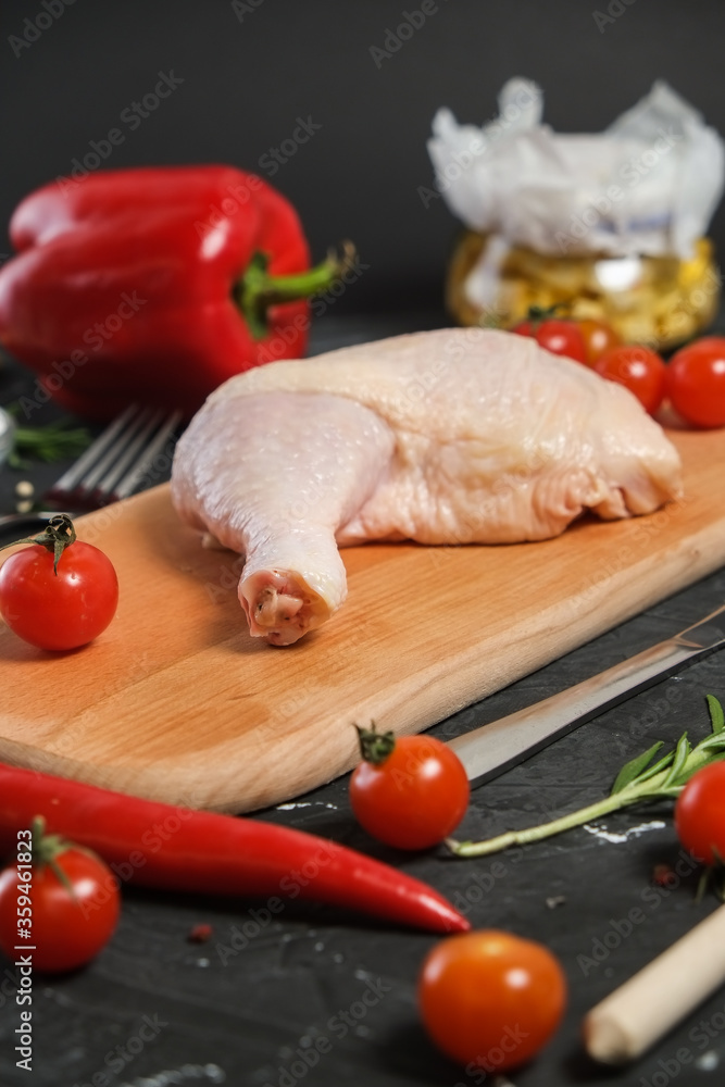 Chicken Leg in a wooden Cutting board, fresh rosemary, fresh cherry tomatoes, fresh chili peppers, garlic, lime and sea salt on a black background. Chicken Leg in a wooden Cutting board, fresh rosemary, fresh cherry tomatoes, fresh chili peppers, garlic, lime and sea salt on a black background.