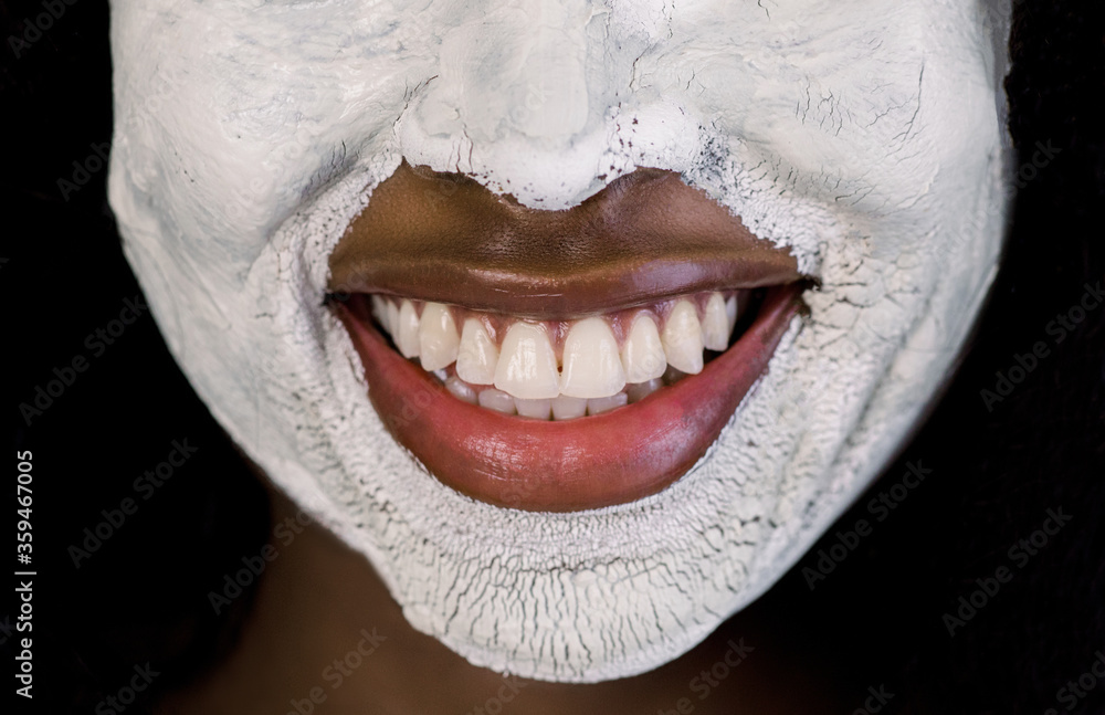 Fototapeta premium Facial treatment, mud clay cleansing mask. Cropped close up image of half of face of beautiful African woman with white clay facial mask on face. Nice smile of charming woman with facial mask