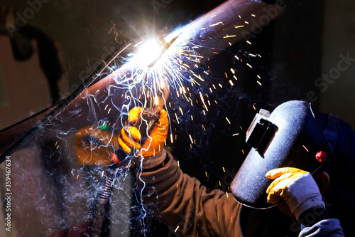 The welder is welding to a steel plate. Welding is the process of joining two plastic or metal parts by melting them with or without using a further molten material. © Funtay