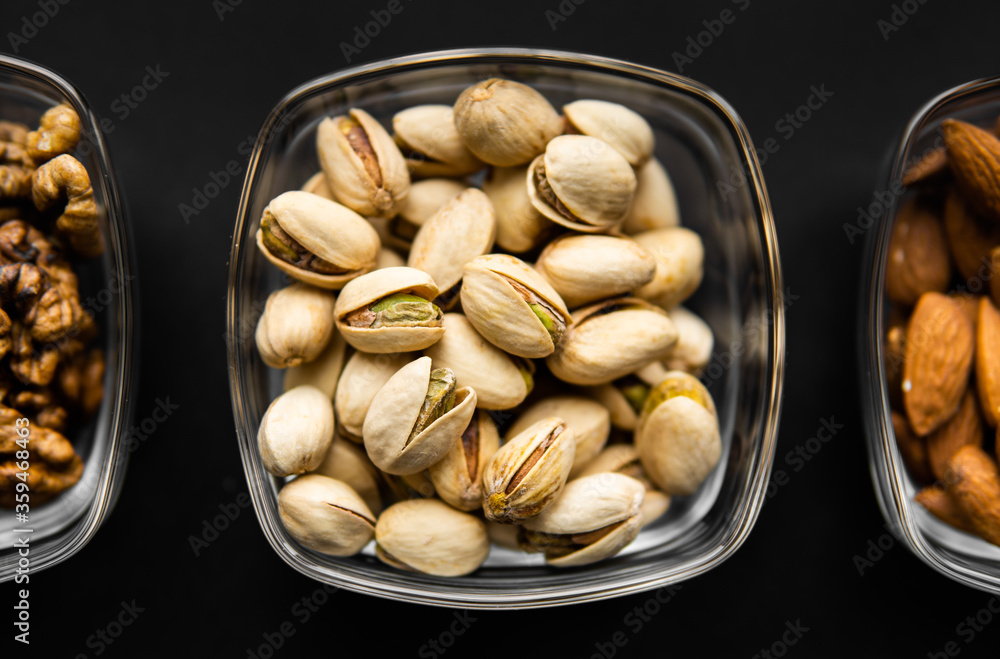 Almond, pistachio and walnut in a small plates which standing on a black table. Nuts is a healthy vegetarian protein and nutritious food. Almond, pistachio and walnut in a small plates which standing on a black table. Nuts is a healthy vegetarian protein and nutritious food.