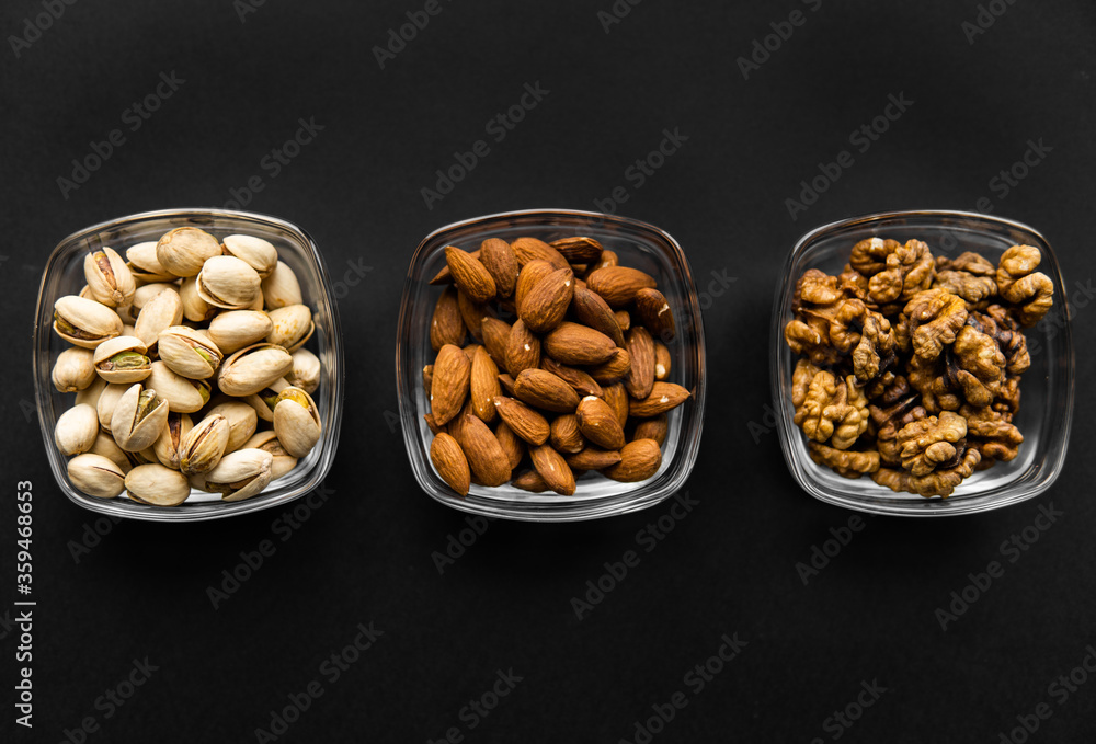Almond, pistachio and walnut in a small plates which standing on a black table. Nuts is a healthy vegetarian protein and nutritious food. Almond, pistachio and walnut in a small plates which standing on a black table. Nuts is a healthy vegetarian protein and nutritious food.