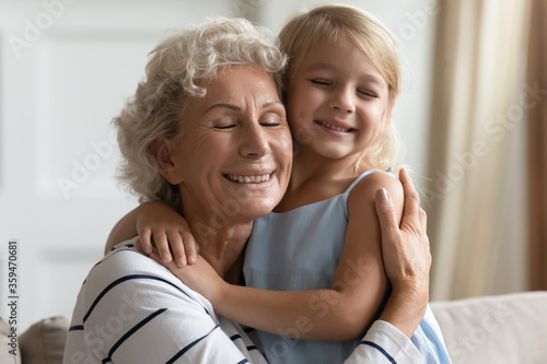 Close up view loving grandmother cuddle snuggle to small granddaughter people closed eyes enjoy tender moment express cherish and sincere affection, sit on sofa in living room, love protection concept