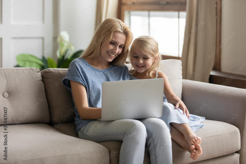 Nanny and little girl spend time in internet, sit on couch mom and small daughter watch educational program app for juniors, e-commerce users buy services on-line, have fun use pc modern tech concept