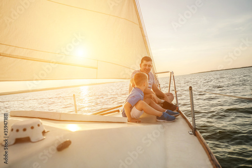 Happy traveler father and son enjoying sunset from deck of sailing boat moving in sea at evening time. Bonding Travel, Summer, Holidays, Journey, Trip, Lifestyle, Yachting concept.