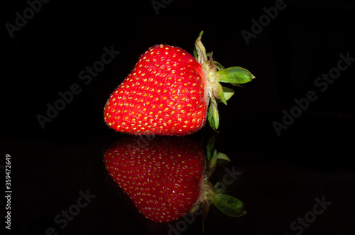 One strawberry isolated on a black background with mirror reflection.