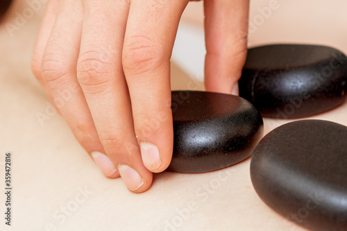 Back massage on back of woman with black hot stones close up.