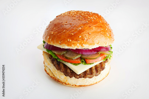 Juicy burger with onion rings, cucumbers, lettuce, cheese on a white background
