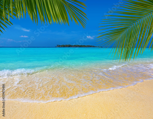 Fototapeta Naklejka Na Ścianę i Meble -  palm leaves over a sandy tropical beach, turquoise sea and island in the background, Maldives