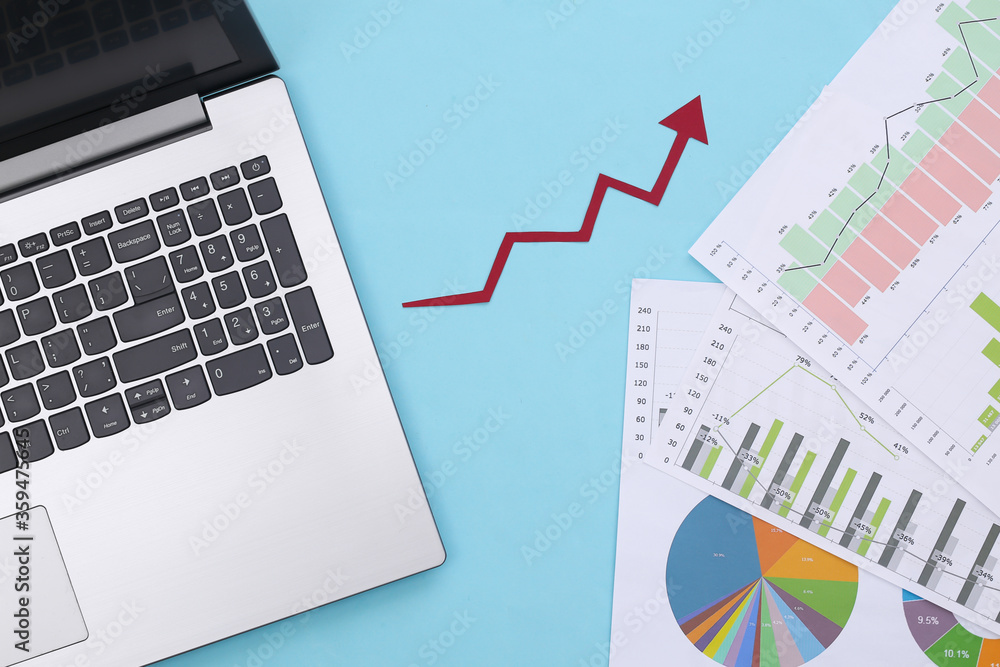 Growth upward arrow, graphs and charts with laptop on a blue background. Online business. Business success. Top view Growth upward arrow, graphs and charts with laptop on a blue background. Online business. Business success. Top view