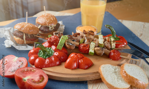 spring vegetables - bell peppers, cucumbers, onions, lettuce, tomato with grilled kebabs and orange juiceon a blue tablecloth photo